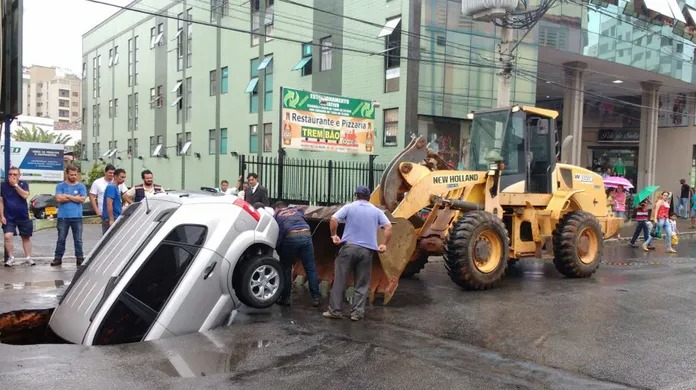 Na foto vemos um carro afundado no asfalto após pista ceder no centro de Viçosa.