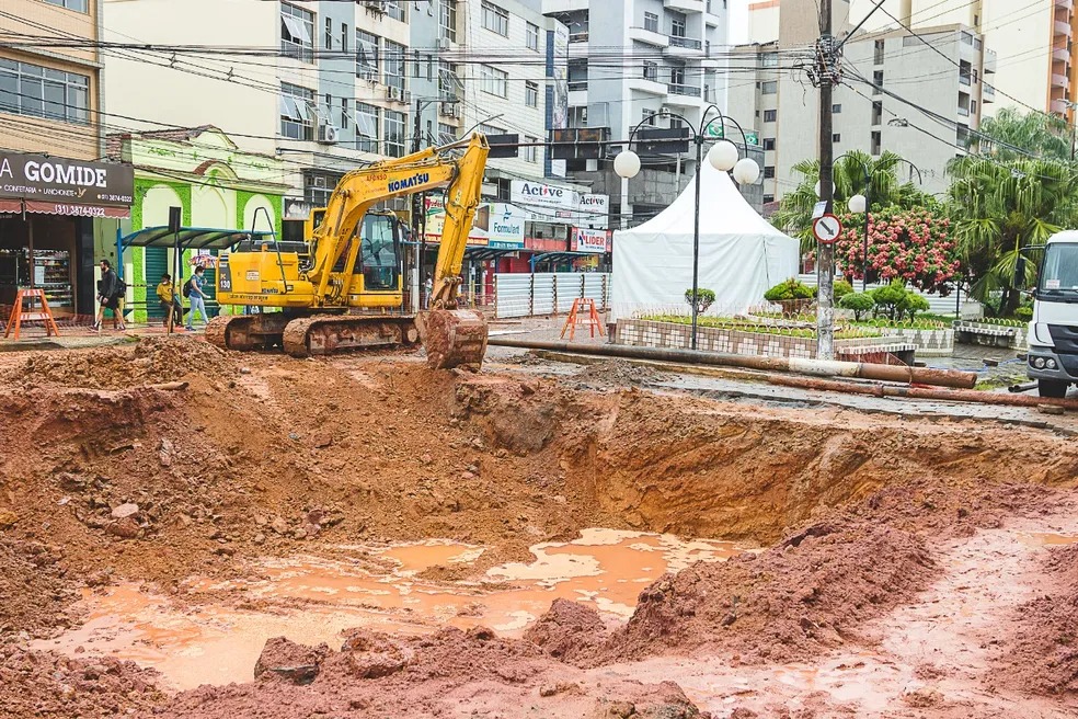 Na foto, uma máquina trabalha sobre uma cratera na  Praça Doutor Mário del Giudice em trecho danificado sobre a galeria do córrego da Conceição em Viçosa.